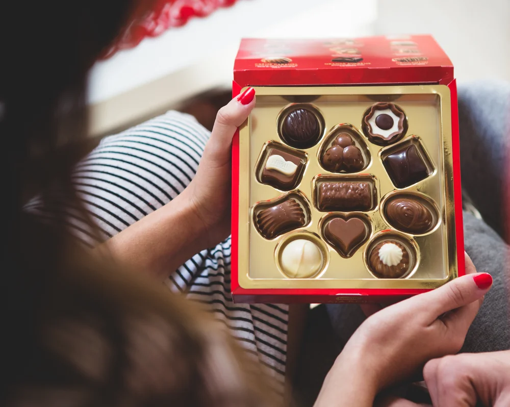 Hands holding an open box of assorted chocolates